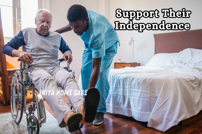Dedicated male caregiver from Iniya Home Care in Pollachi helping a senior man in a wheelchair at home, supporting mobility
